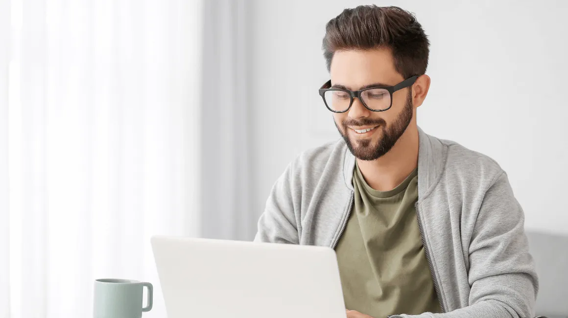 Mężczyzna w okularach pracuje przy laptopie, uśmiechając się do ekranu